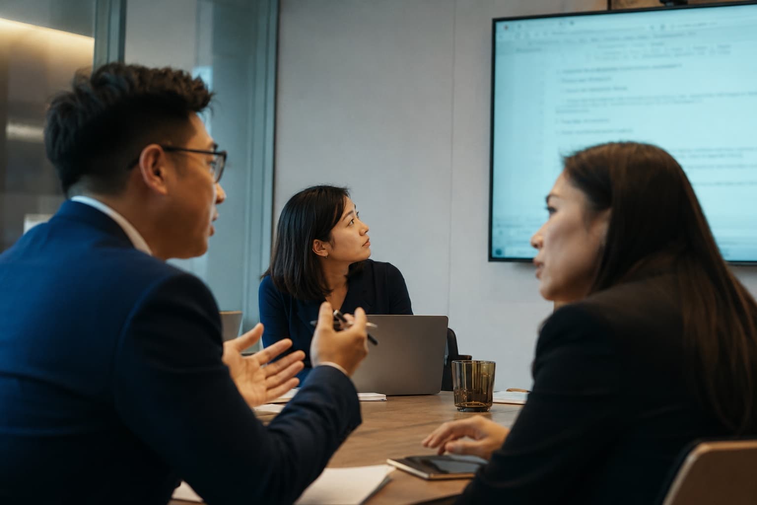 會議室裡的團隊對齊：三人圍桌討論、螢幕上是共享文件
